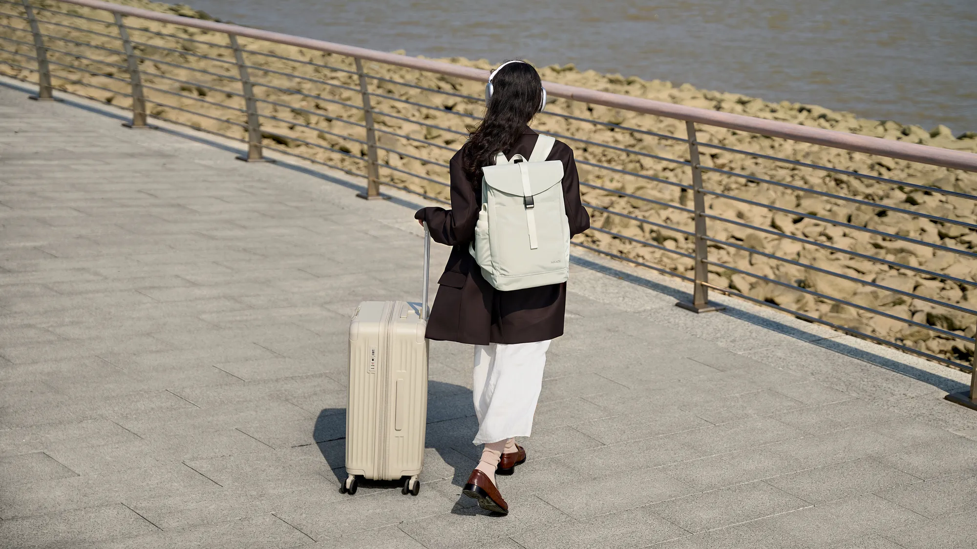 A traveller walking with an MRACE backpack and a suitcase